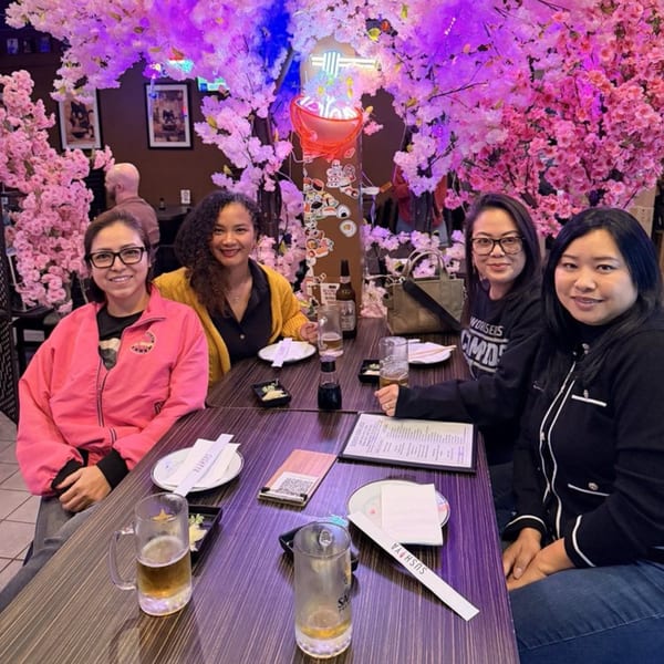 Four women smiling at a table in Sushiya, surrounded by pink cherry blossom decor.