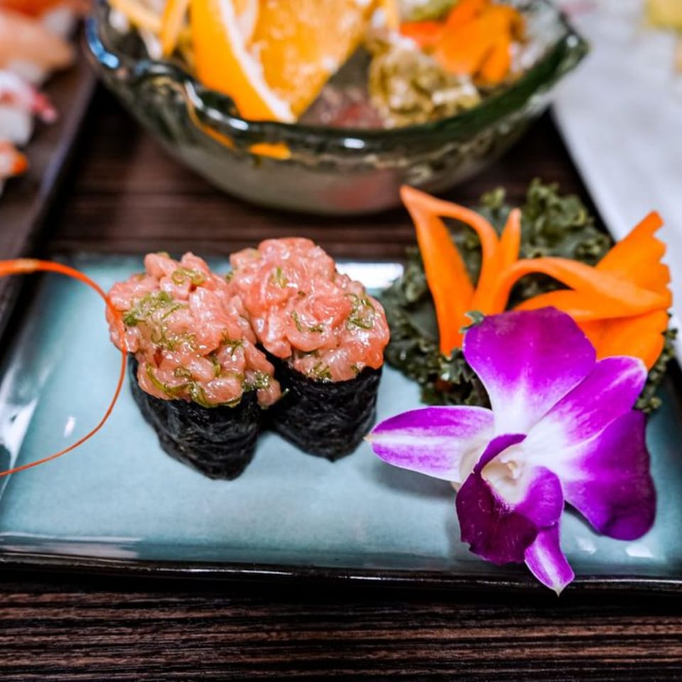 Two gunkan maki sushi with spicy tuna, garnished with a purple orchid and carrot slices.