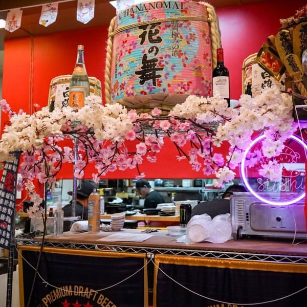 Japanese restaurant counter with cherry blossom decorations, sake barrels, and a neon sushi sign.