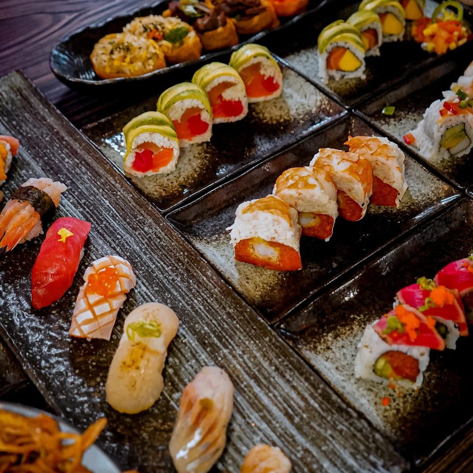 Assortment of colorful sushi rolls and nigiri on dark rectangular plates at Sushiya.